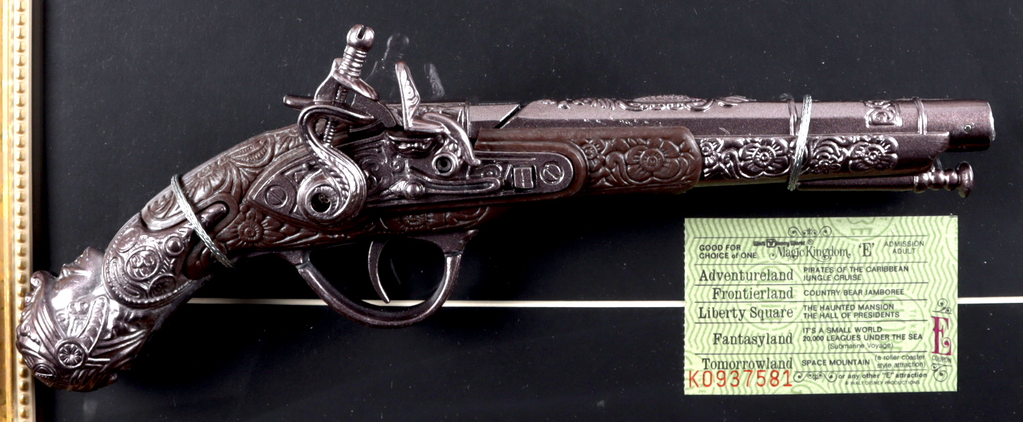Disney World "Pirates of the Caribbean" 15x26 Custom Framed Print with Pirates of the Caribbean Souvenir Gun & "E" Vintage Pirates Ride Ticket at PristineAuction.com Disney World "Pirates of the Caribbean" 15x26 Custom Framed Print with Pirates of the Caribbean Souvenir Gun & "E" Vintage Pirates Ride Ticket at PristineAuction.com